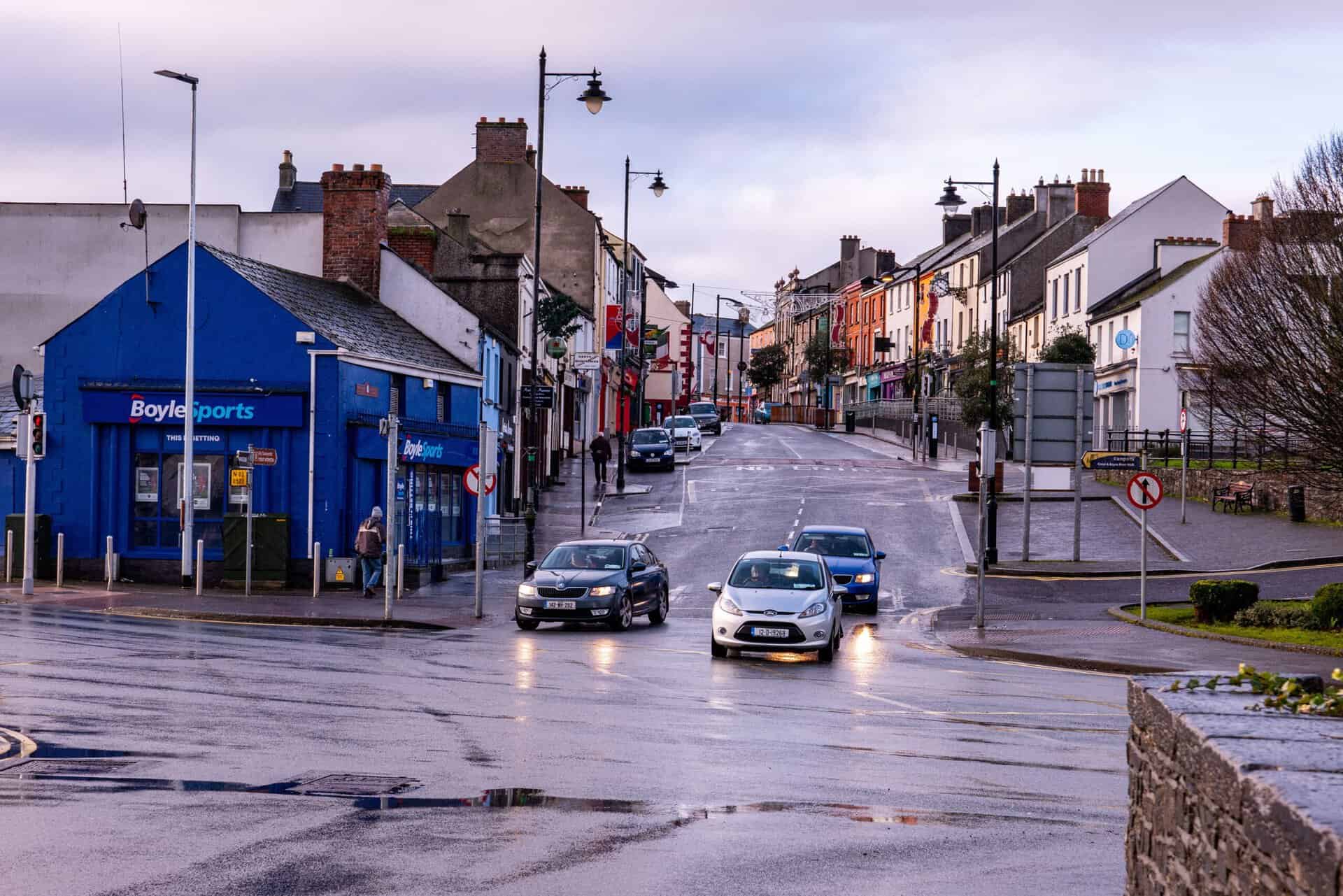Town street in Ireland with shops and cars, rainy weather.