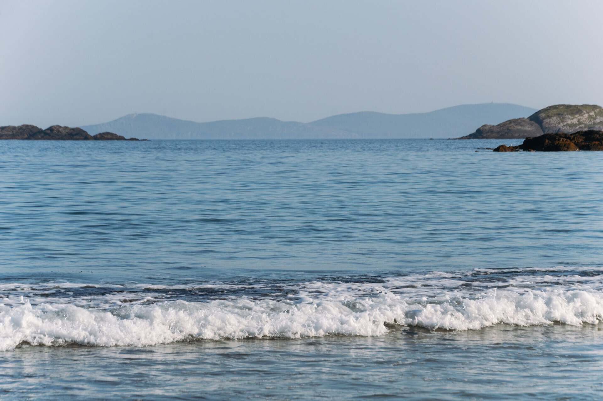 Peaceful view of the Irish coastline with gentle waves and distant hills under a clear sky.